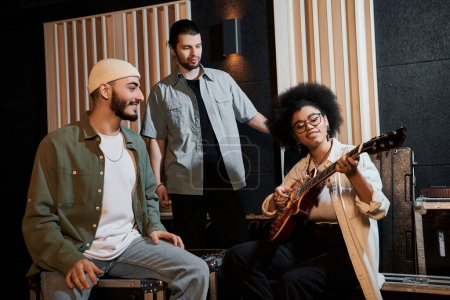 Three individuals sitting in a recording studio, immersed in playing a guitar and creating music together.