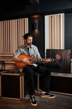 Un guitarrista se sienta en un estudio de grabación, rasgueando su instrumento con enfoque y pasión durante un ensayo de la banda de música.
