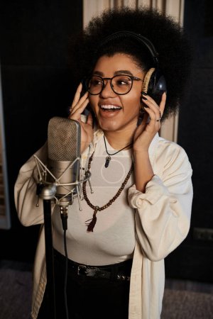 A female musician with afro hair passionately sings into a microphone during a music band rehearsal in a recording studio.