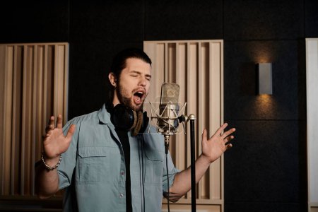 Foto de Un hombre canta apasionadamente en un micrófono en un estudio de grabación durante una sesión de ensayo de la banda de música. - Imagen libre de derechos