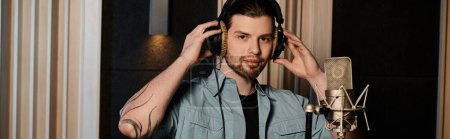 Photo for A man with headphones stands in front of a microphone during a music band rehearsal in a recording studio. - Royalty Free Image