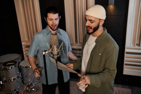 Foto de Dos hombres están uno al lado del otro en un estudio de grabación, colaborando creativamente en la música para el ensayo de su banda. - Imagen libre de derechos
