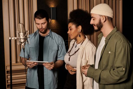 Un groupe de musique dans un studio d'enregistrement examine une tablette ensemble, examine leur travail et discute de leurs prochaines étapes.