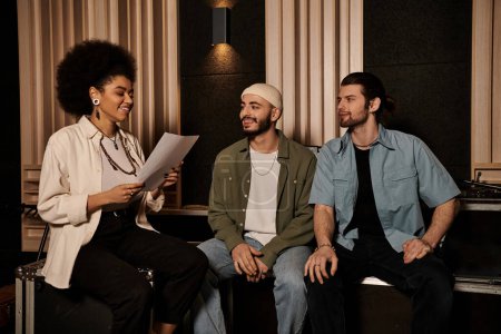 Drei Personen einer Musikband sitzen in einem Tonstudio, vertieft in Gespräche und planen ihr nächstes Musikprojekt.