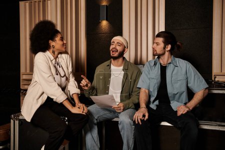 Foto de Tres músicos se sientan en un estudio de grabación, participando en animadas discusiones durante una sesión de ensayo de la banda. - Imagen libre de derechos
