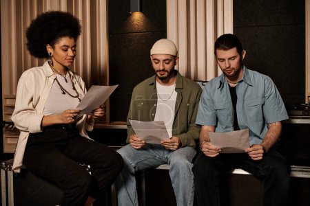 Three people in a recording studio, sitting, focused, reading papers for a music band rehearsal.