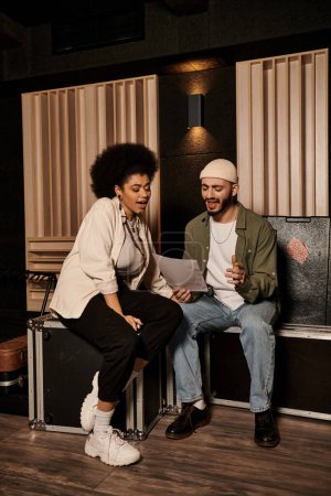 A man and woman are seated in a recording studio, collaborating on music for their bands upcoming performance.