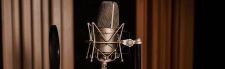 Téléchargez les photos : Un microphone solitaire repose sur une table, prêt à être utilisé dans une répétition d'un groupe de musique dans un studio d'enregistrement. - en image libre de droit