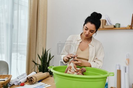 A woman sits at a table, upcycling clothes in front of a green bucket.