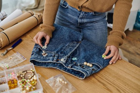 Woman in brown sweater adding beads to jeans.