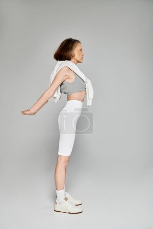 Foto de Una mujer madura en traje cómodo se para con los brazos extendidos, posando activamente. - Imagen libre de derechos