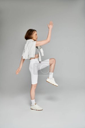 Foto de Una mujer atractiva madura en pantalones cortos blancos y una camiseta blanca posa activamente y hace ejercicios. - Imagen libre de derechos
