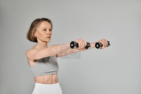 Elderly lady doing dumbbell exercises on gray background.