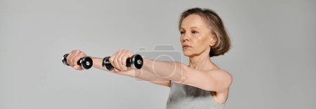 Photo for A mature, attractive woman in active wear confidently holds two dumbbells. - Royalty Free Image