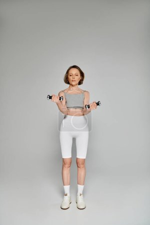 Foto de Una mujer madura y equilibrada en ropa deportiva levanta pesas con determinación. - Imagen libre de derechos