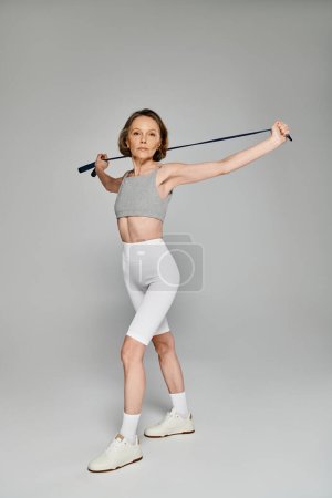 A mature woman in white top and shorts strikes a pose with a ski pole.