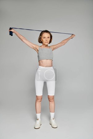 Photo for Mature woman in comfy attire exercises with resistance band. - Royalty Free Image