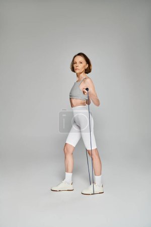 Téléchargez les photos : Mature woman in active wear holding skipping rope against white background. - en image libre de droit