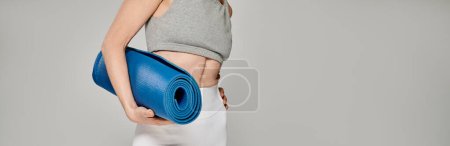 Mature woman in relaxed pose holding a blue yoga mat.