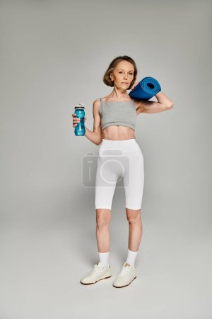 Téléchargez les photos : Femme forte dans des vêtements confortables tenant un tapis de yoga et une bouteille d'eau. - en image libre de droit