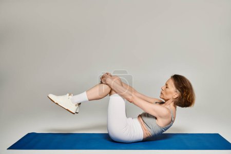 Foto de Una mujer madura y atractiva en cómodos ejercicios de atuendo activamente en una alfombra azul. - Imagen libre de derechos
