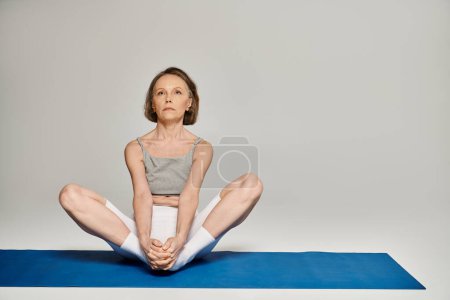 Mature woman in yoga pose on blue mat.
