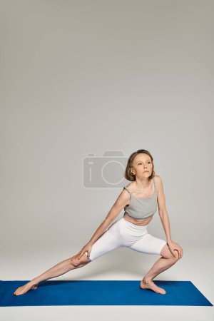 Una mujer madura y atractiva practicando yoga con gracia en una esterilla azul.