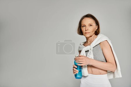 Ältere Frau in bequemer Kleidung nippt gelassen an einer Wasserflasche.