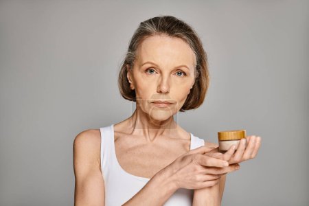 Foto de A mature, attractive woman in casual attire holds a container of cream. - Imagen libre de derechos
