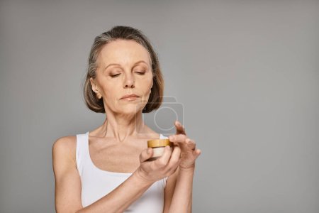Photo for A mature woman in comfy attire gracefully holds a container of cream. - Royalty Free Image