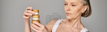 Photo for A mature, attractive woman in casual clothing gracefully holds up a bottle of cream. - Royalty Free Image