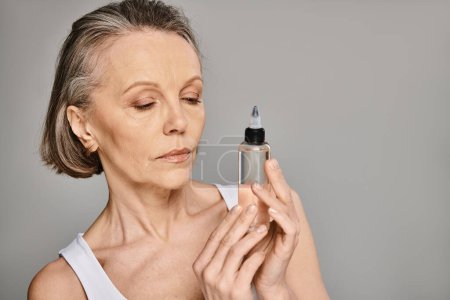 A mature woman gracefully holds a skin care product bottle.