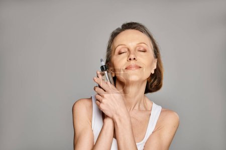 Photo for Woman in casual wear peacefully holding serum with closed eyes. - Royalty Free Image
