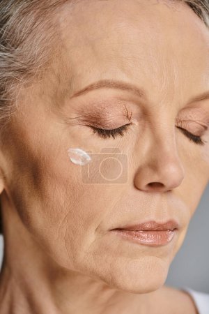 Téléchargez les photos : Une femme mûre appliquant de la crème sur son visage pour une routine rajeunissante de soins de la peau. - en image libre de droit