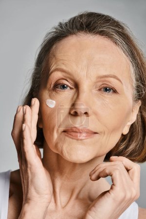 An elegant older woman gently applying cream to her face.