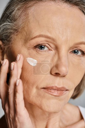 Eine elegante ältere Frau cremt ihr Gesicht sanft ein und pflegt ihre Haut.