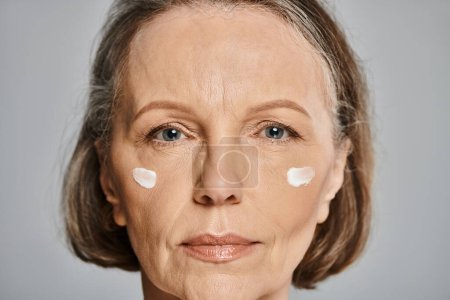 Mature woman gracefully embraces the soothing effects of facial cream.