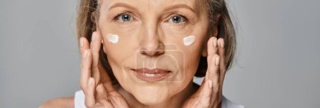 Foto de Una mujer elegante se aplica suavemente crema en la cara para una rutina de cuidado de la piel rejuvenecedora. - Imagen libre de derechos