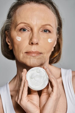 Una mujer madura aplicando suavemente un tazón de crema en su cara.