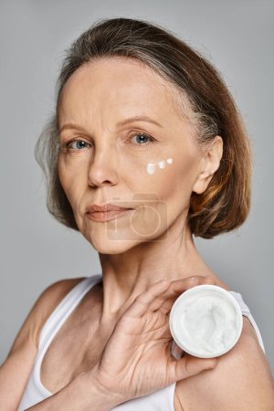 Woman in comfortable attire actively applying cream to her face.