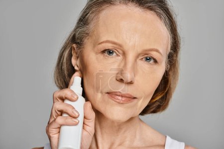 A mature woman in comfy attire actively cleanses her face with a facial cleanser.