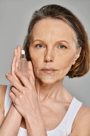 Photo for Mature woman in activewear holding a bottle of skin care product. - Royalty Free Image