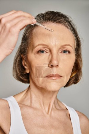A woman carefully applies a serum to her face, focusing on her skincare routine.