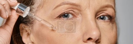 Photo for A mature woman in comfy attire is applying serum to her face - Royalty Free Image