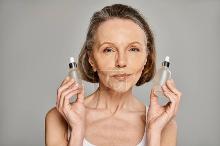 A mature, attractive woman elegantly holds two bottles of skin care products.