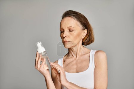 Une femme mûre tient gracieusement une bouteille de lotion.