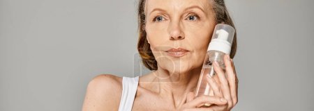 Photo for A mature woman gently cleanses her face with a facial cleanser, maintaining a beauty routine. - Royalty Free Image