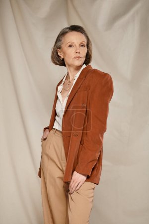 Une femme mûre dans un blazer brun et un pantalon bronzé, respirant la confiance et le style, s'engage dans des poses actives.