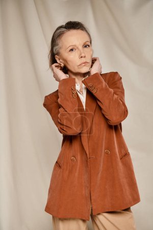Téléchargez les photos : Élégante dame âgée en blazer bronzé et pantalon pose élégamment tout en exerçant. - en image libre de droit