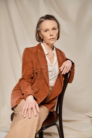 Téléchargez les photos : Femme élégante assise sur une chaise en blazer bronzé et pantalon, exsudant grâce et confiance. - en image libre de droit